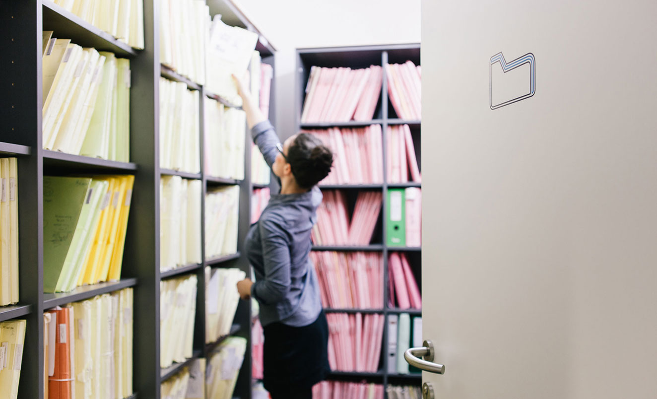 Woman standing in room full of bookshelves filled with files