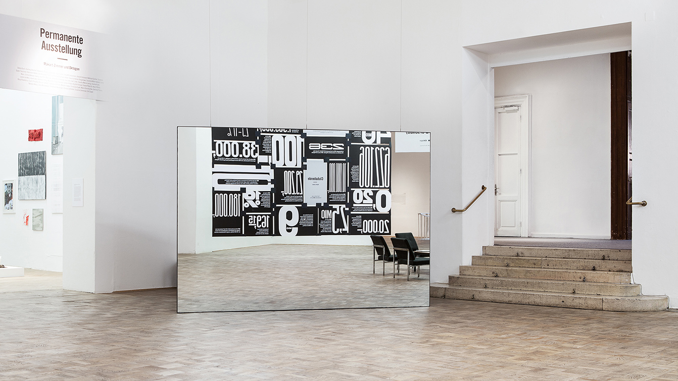 A large mirror standing in the exhibition space reflecting the room filling exhibition graphics