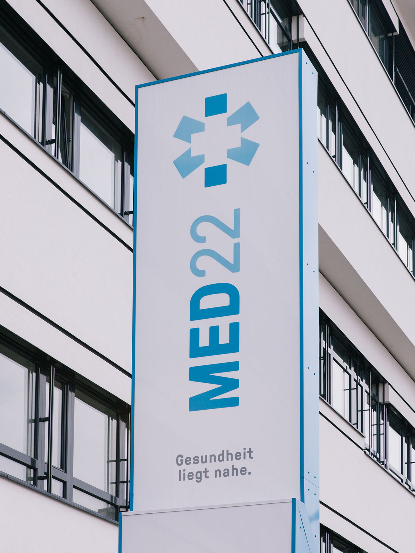 Stele in front of the health center, white rectangle with blue borders and the corporate with lettering and logo in blue
