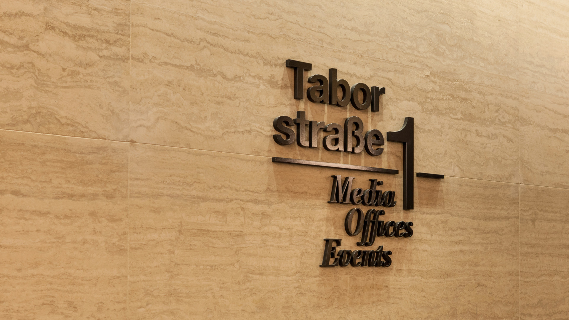 Logo auf Marmorwand angebracht - schwarzer Schriftzug mit Trennstrich: Taborstraße 1, Media, Offices, Events