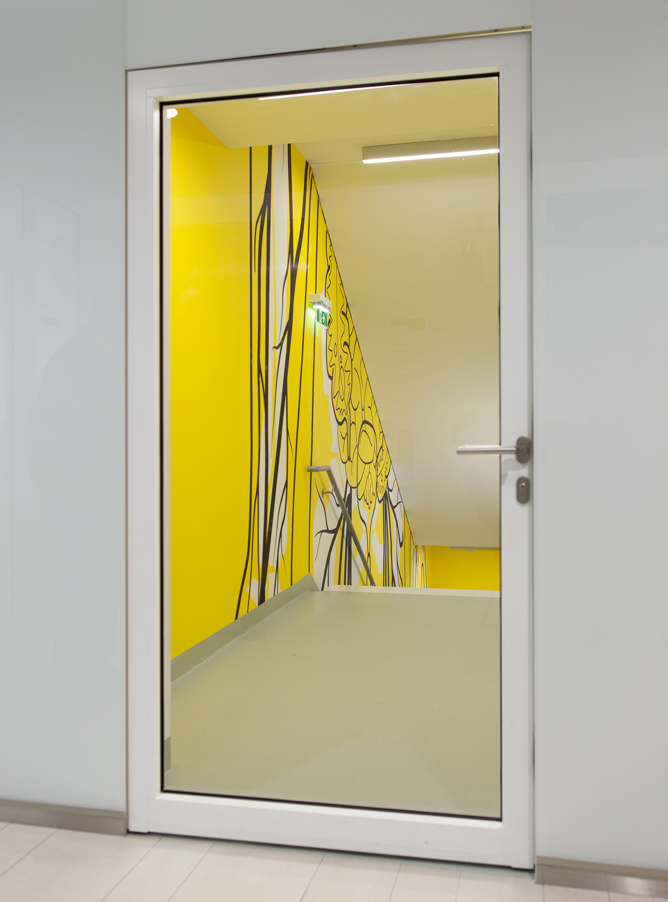 Glastüre zum Gang mit Blick in das Stiegenhaus mit gelben Wänden und schwarzen Illustrationen