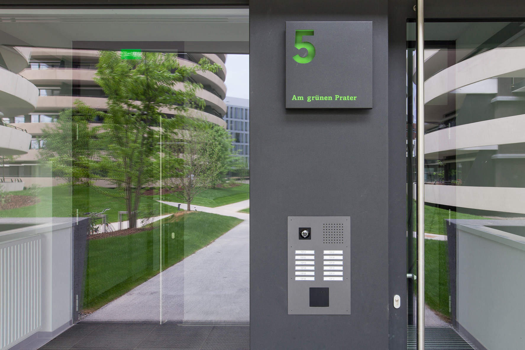 Entrance area to a building with glass door, bell sign and door lettering with punched out stencil lettering and house number, gray with green background