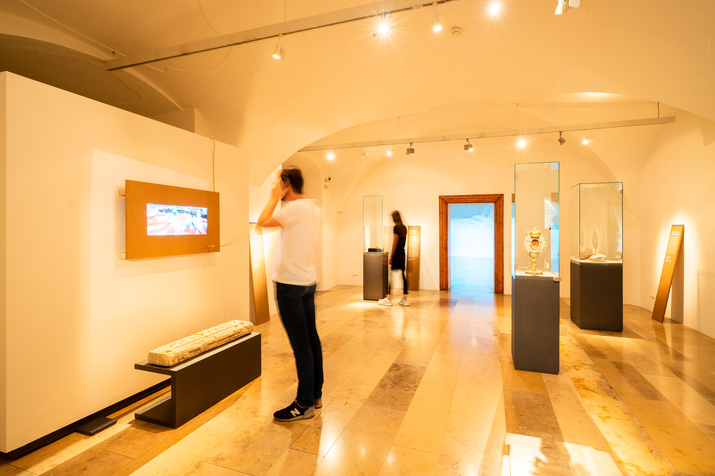 Exhibition space with objects and a screen embedded in MDF panels, in front of which a man stands