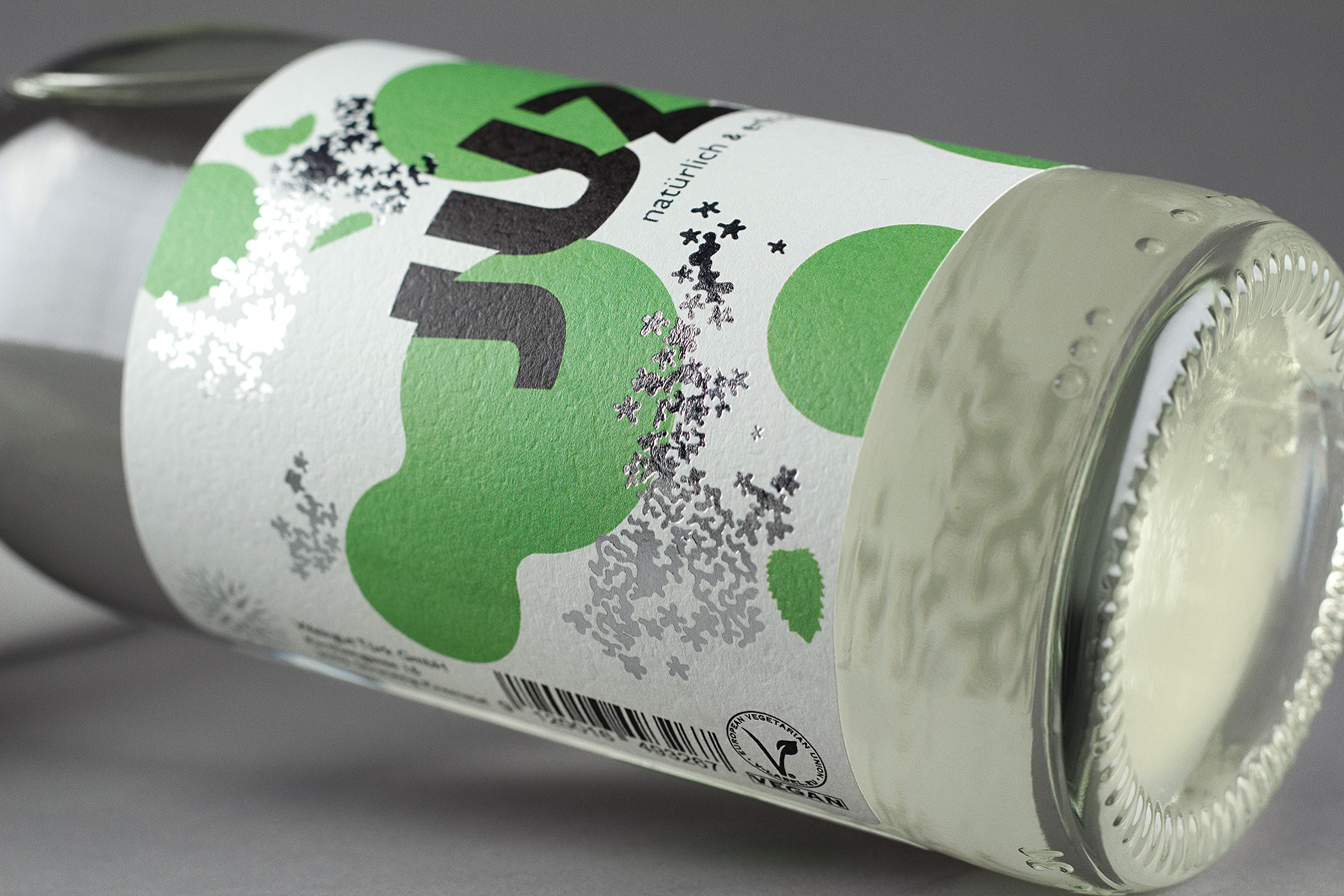 Detailansicht einer Flasche des Erfrischungsgetränks Juzzz: silberne Folie auf Etikettenpapier mit grünen Punkten