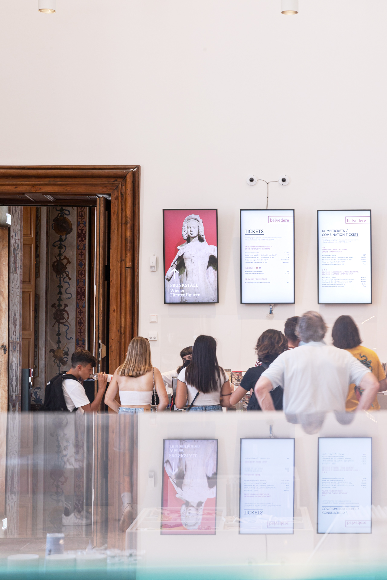Menschen vor einer Türe stehend, neben der verschiedene digitale Displays mit Ausstellungsinformationen installiert sind