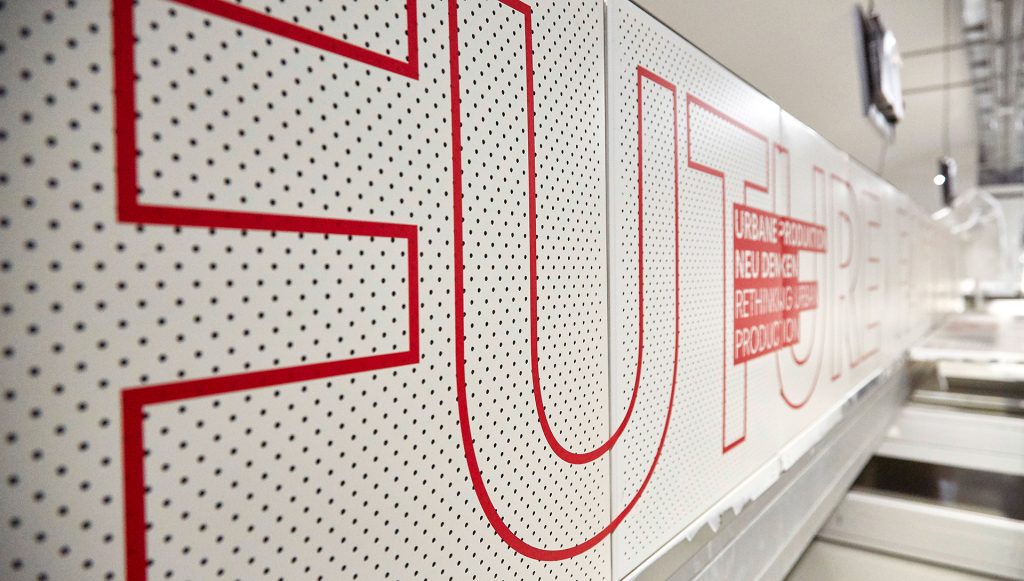 Exhibition display of white ceiling panels with printed red lettering "Future Factory"